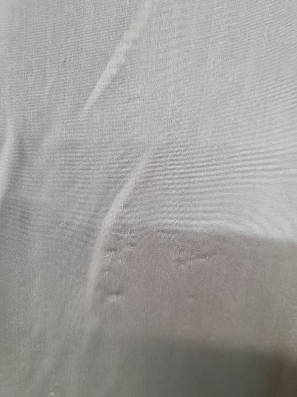 A close-up of a light gray or off-white textured fabric surface with soft folds and shadows.