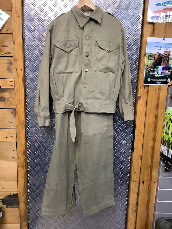 Green military-style jacket and pants hanging on a wooden surface with a patterned wall in the background.