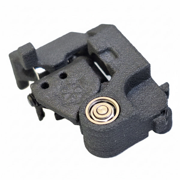 A black textured metal mechanical component, likely a firearm magazine or receiver part, featuring a gold-toned bearing visible on one side, isolated on a white background.