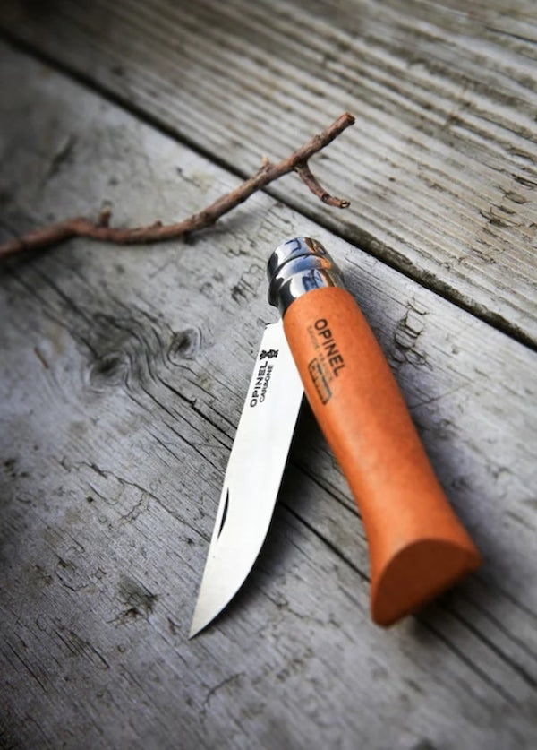 Orange folding knife with silver blade on a wooden surface