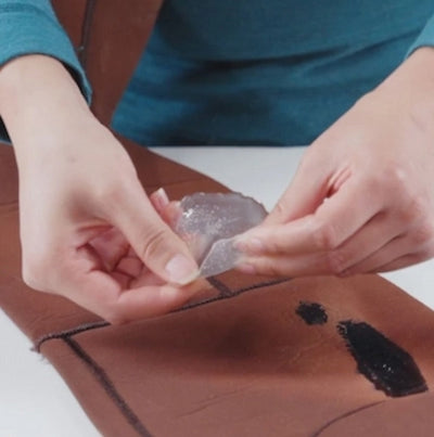 Person applying a patch to a leather surface with a visible stain.