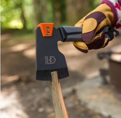 Hand holding a black axe with orange handle in a forest setting