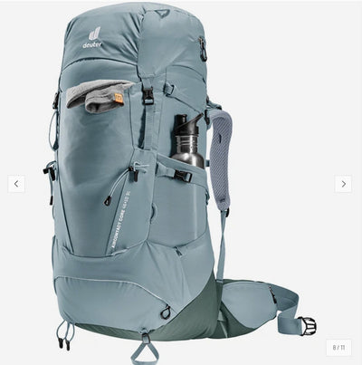 A Deuter hiking backpack in a muted slate blue-gray color, shown from a three-quarters angle against a light gray background. The backpack features multiple zippered compartments, a side water bottle pocket holding a silver bottle, and padded shoulder straps.
