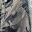 Camouflage jacket with 'OPS/GEAR' logo on a metallic surface