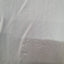 A close-up of a light gray or off-white textured fabric surface with soft folds and shadows.