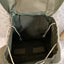 Green backpack with open lid showing interior compartments on a textured surface