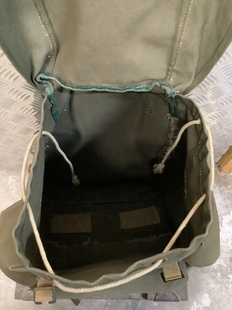 Green backpack with open lid showing interior compartments on a textured surface
