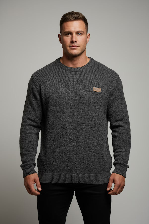 Man wearing a gray sweater with a small logo on a gray background