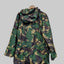 A hooded camouflage jacket with a green, black, and tan pattern, hanging on a wooden hanger against a solid gray background.