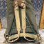 Green backpack with brown leather straps on a textured wall background