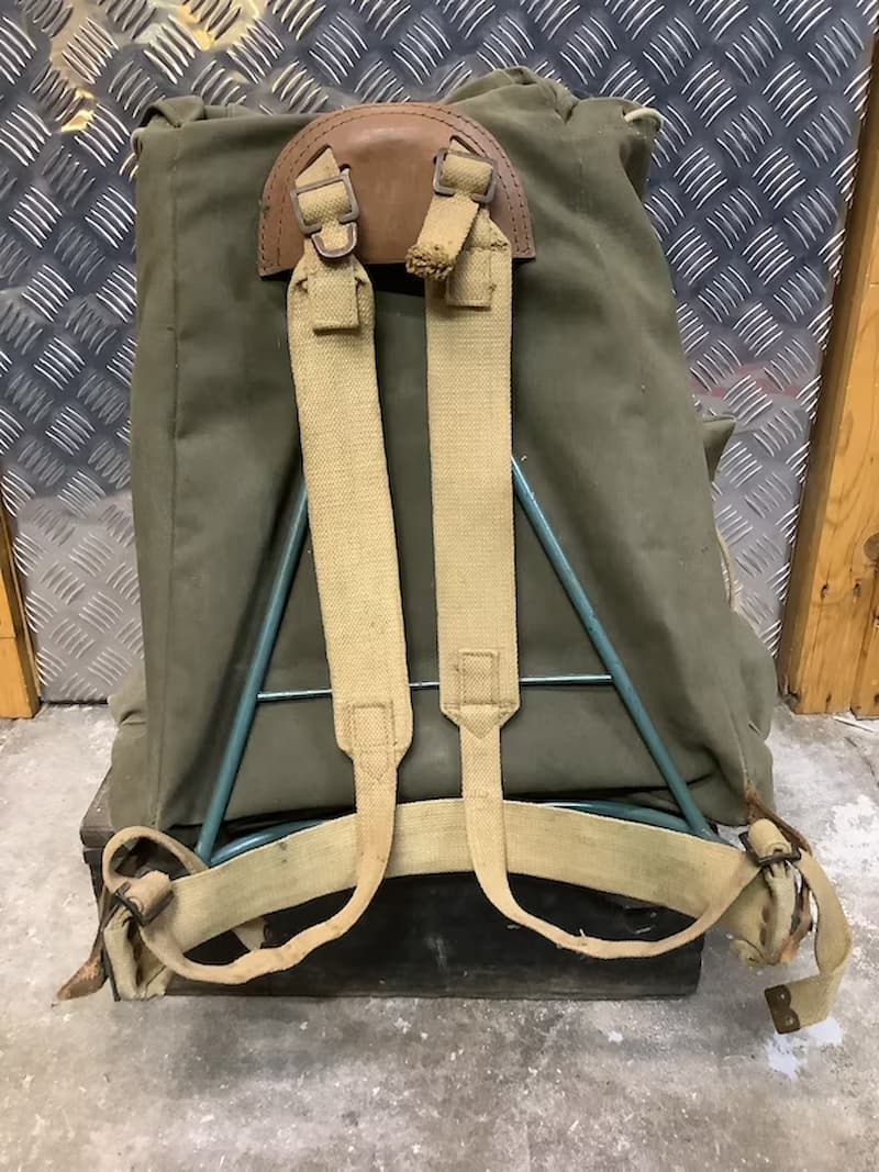 Green backpack with brown leather straps on a textured wall background