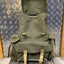 Green backpack with brown straps on a metal platform against a patterned wall.