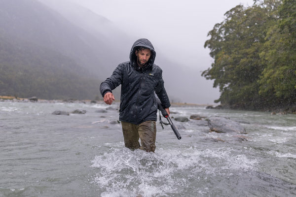 Person wading through a river wearing a raincoat on a foggy day.