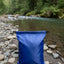 Blue bag on a rocky riverbank with green forest in the background