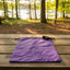 Purple drawstring bag on a wooden picnic table with a forest and lake background