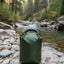 Green waterproof bag on a rock by a forest stream