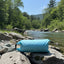 Blue inflatable raft on rocks by a river with trees and mountains in the background