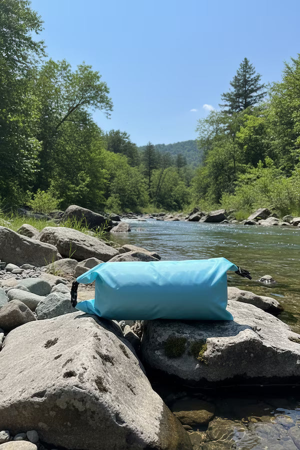 Blue inflatable raft on rocks by a river with trees and mountains in the background