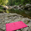 Pink mat on a rocky riverbank with green trees in the background