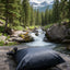 Black inflatable pillow on a rock by a stream with trees and mountains in the background