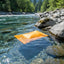 Orange fabric floating in a clear river with trees and mountains in the background