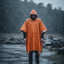 Person wearing an orange rain poncho standing in the rain with a product box on the ground.