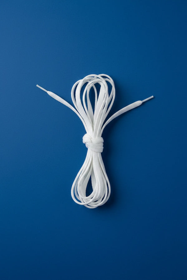 A coiled bundle of white shoelaces tied in the center, photographed flat against a solid blue background.
