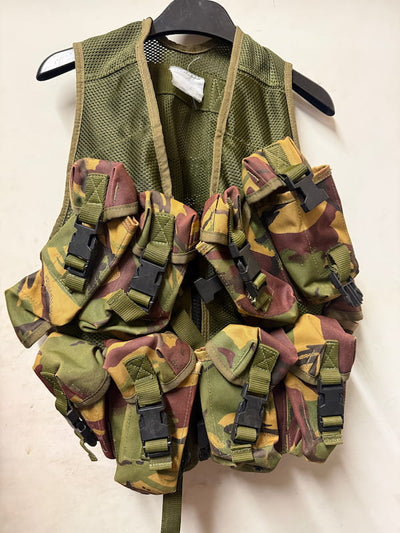 A military-style tactical vest with multiple camouflage pouches and straps, hanging on a black hanger against a plain off-white background.