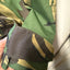 Close-up of a camouflage-patterned garment sleeve with a dark brown cuff tab, held by a hand against an indoor background.