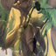 Close-up of a camouflage-patterned garment, likely a jacket or overshirt, featuring green, tan, and dark brown camo print with a snap button and drawstring closure.