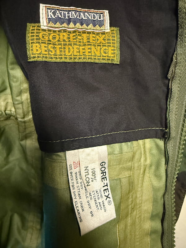 Close-up of the interior collar of a jacket showing a Kathmandu GORE-TEX Best Defence label and a white GORE-TEX tag on olive green and black fabric.