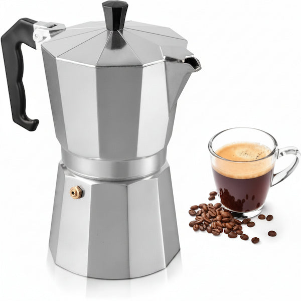 A classic stainless steel moka pot with a black handle and lid knob, shown next to a glass cup of espresso and scattered coffee beans on a white background.