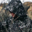 Person wearing a camouflage jacket with a logo in a natural setting