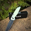 Folding knife with a green handle on a stone surface next to RUIKE packaging.