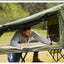 Man setting up a green camping cot outdoors in a natural setting