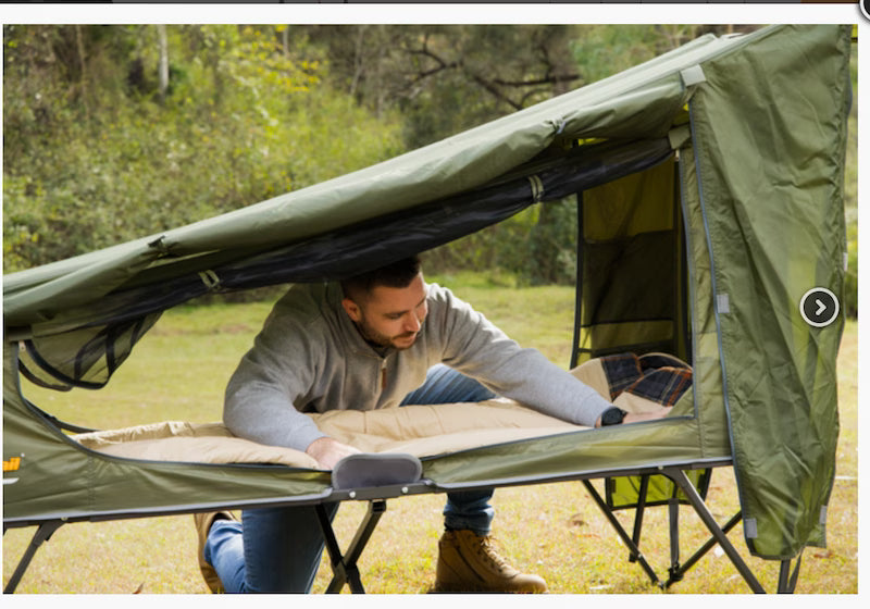 Man setting up a green camping cot outdoors in a natural setting