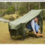 Man sitting on a green camping cot by a river with trees in the background