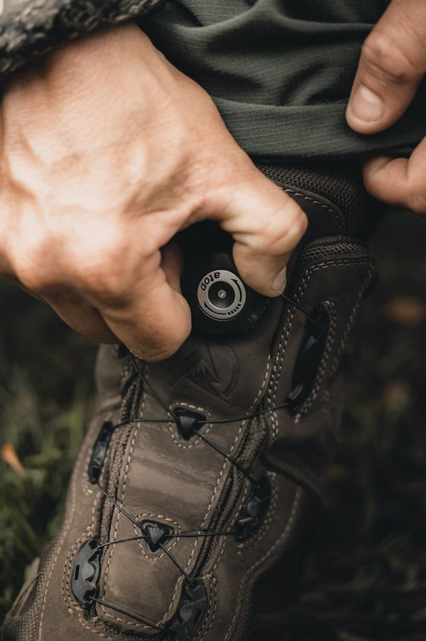 Close-up of a person adjusting the laces on a brown hiking boot with a blurred natural background.