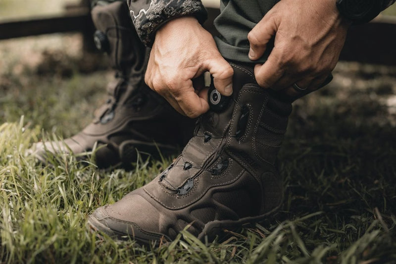 Person tying a boot in a grassy area