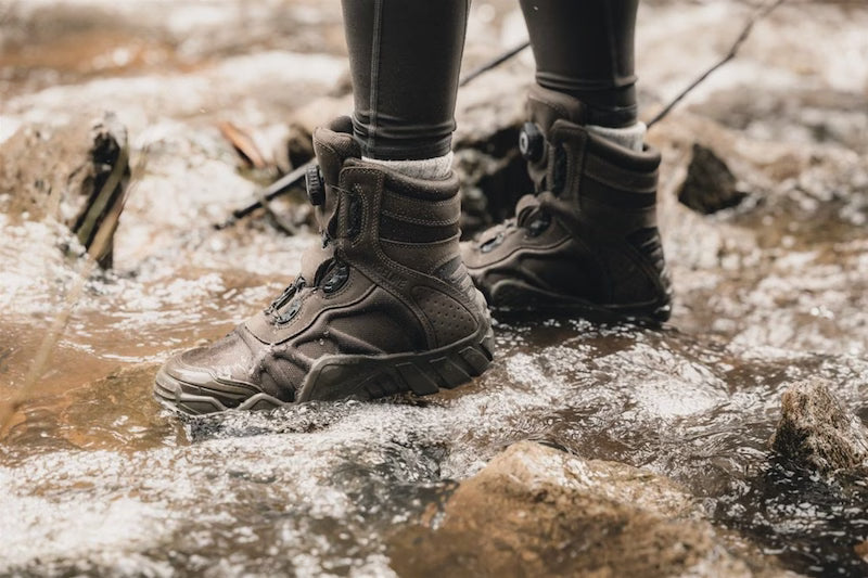Person wearing brown boots walking through a shallow stream.