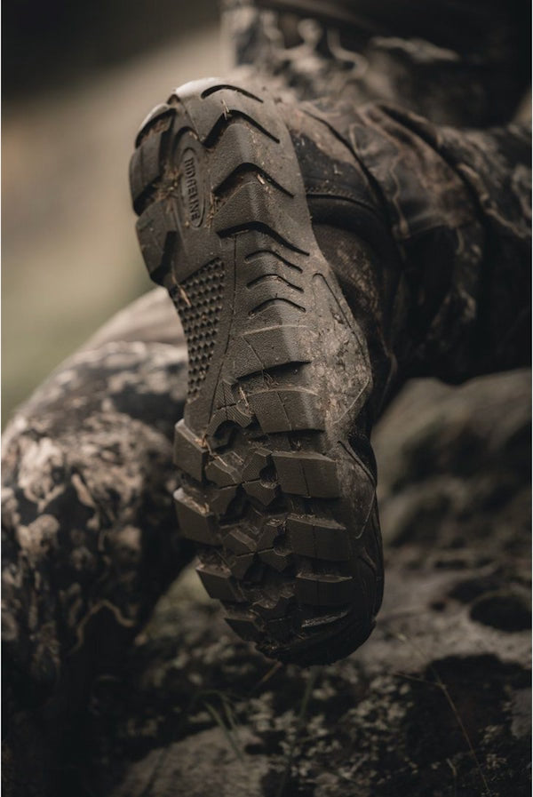 Close-up of a rugged boot with a textured sole on a camouflage-patterned background