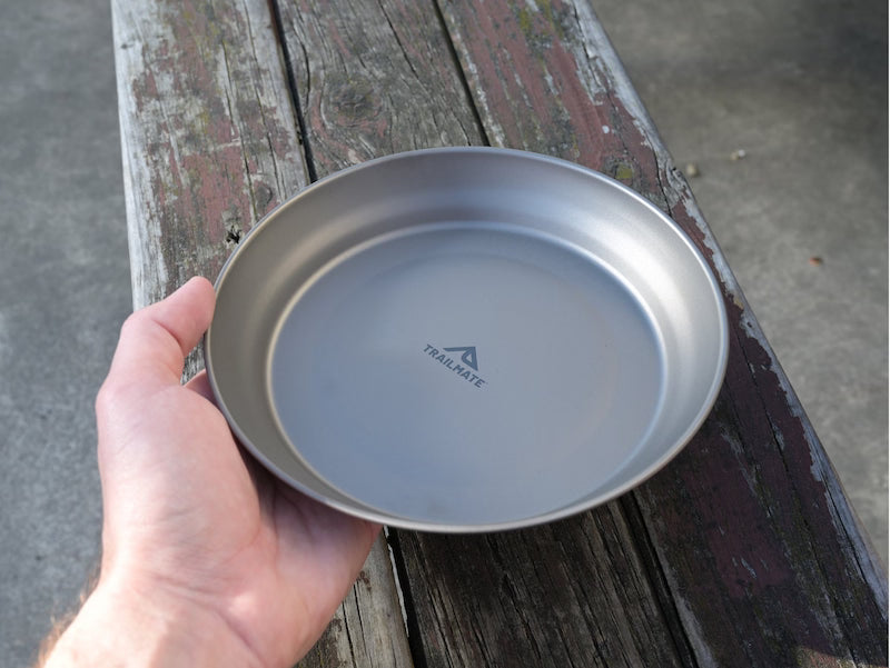 Hand holding a metallic plate with a brand logo on a wooden surface