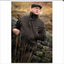 Man in a dark jacket and cap standing by a stone wall with a natural background