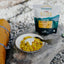 Campfire meal with a bowl of food and a 'Back Country Elite' package on a rocky surface.