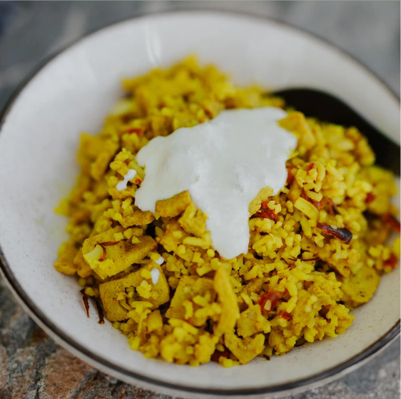 Yellow rice dish with a dollop of white sauce in a white bowl.