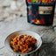  bowl of food with a spoon on a wooden surface, with a package in the background