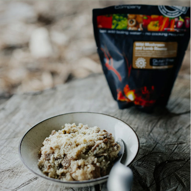 Mushroom and wild herb risotto in a bowl with a package of risotto in the background on a wooden surface.