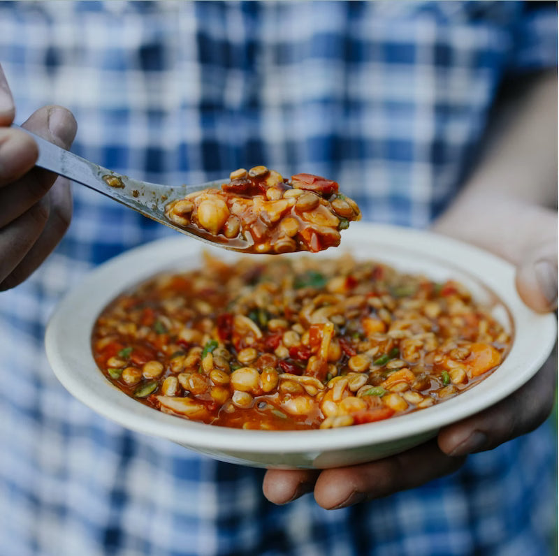 Person holding a bowl of bean stew with a spoonful above