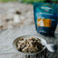 Bowl of food with a spoon on a wooden surface, with a package in the background.
