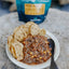 Bowl of chili with tortilla chips on a stone surface, with a blue bag in the background.